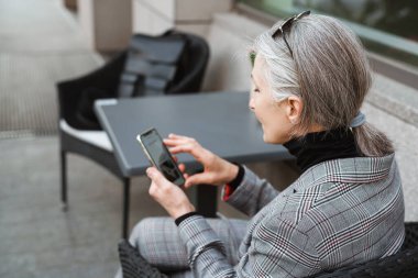 Kafede otururken cep telefonu kullanan son sınıf öğrencisi gri beyaz bir kadın.