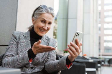 Kafede otururken cep telefonu kullanan son sınıf öğrencisi gri beyaz bir kadın.
