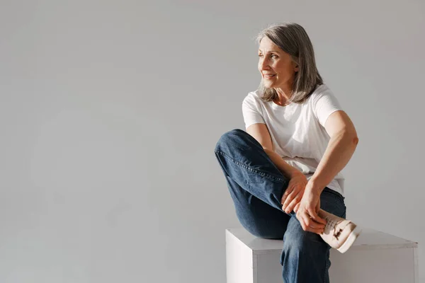 Mulher Sênior Cinza Jeans Sorrindo Enquanto Sentada Caixa Isolada Sobre — Fotografia de Stock