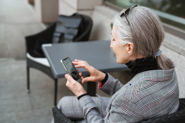 Kafede otururken cep telefonu kullanan son sınıf öğrencisi gri beyaz bir kadın.