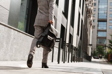 Sokakta yürürken takım elbiseli beyaz kadın çanta taşıyor.