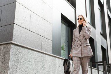 Şehir caddesinde yürürken cep telefonuyla konuşan son sınıf beyaz kadın.