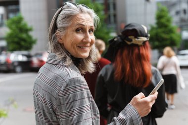 Sokak ortasında yürürken cep telefonu kullanan son sınıf beyaz kadın.