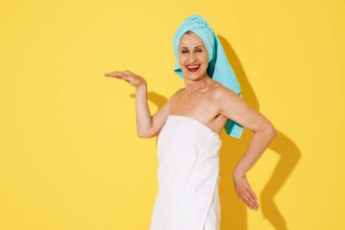 Sarı duvarın üstünde eğlenirken havluyla gülen yaşlı bir kadın.