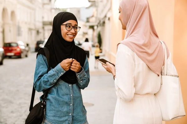 在城市街道上说话时 年轻的穆斯林妇女戴着头巾笑着 — 图库照片