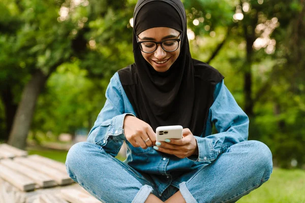 Šťastná Mladá Muslimka Hidžábu Sedí Lavičce Pomocí Mobilního Telefonu — Stock fotografie