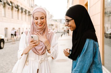 Çok ırklı müslüman kadınlar tesettür takıyor. Şehir caddesinde cep telefonu kullanırken konuşuyorlar.