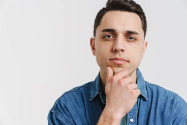 Genç esmer beyaz adam poz veriyor ve beyaz arka planda izole edilmiş kameraya bakıyor.