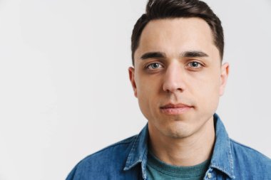 Genç esmer adam poz veriyor ve beyaz arka planda izole edilmiş kameraya bakıyor.