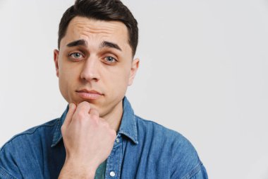 Genç esmer beyaz adam poz veriyor ve beyaz arka planda izole edilmiş kameraya bakıyor.