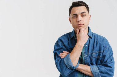 Genç esmer beyaz adam poz veriyor ve beyaz arka planda izole edilmiş kameraya bakıyor.