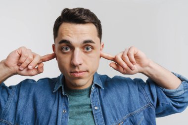 Genç esmer adam kameraya bakıyor ve beyaz arka planda kulaklarını tıkıyor.