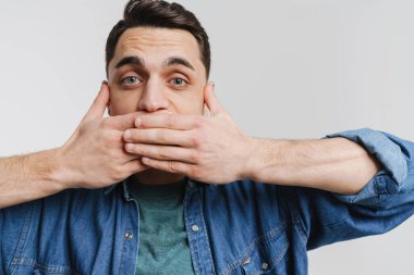 Genç esmer adam beyaz arka planda ağzını kapatan kot gömlekli adam.