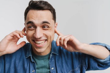 Genç esmer adam gülümsüyor ve kulaklarını tıkıyor.