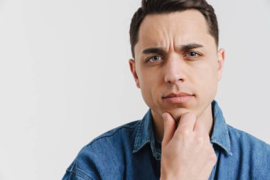 Genç esmer adam somurtuyor ve beyaz arka planda izole edilmiş kameraya bakıyor.