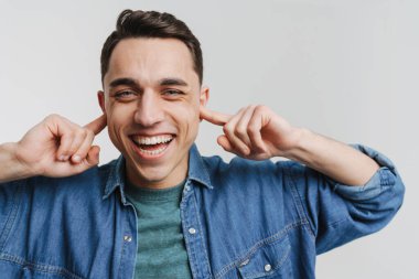 Genç esmer adam gülümsüyor ve kulaklarını tıkıyor.