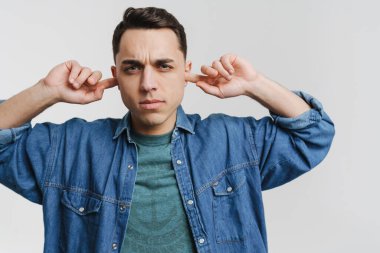 Genç esmer adam kaşlarını çatıyor ve kulaklarını tıkıyor.