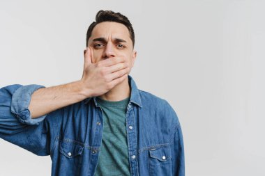Genç esmer adam ağzını kapatıp beyaz arka planda izole edilmiş kameraya bakıyor.