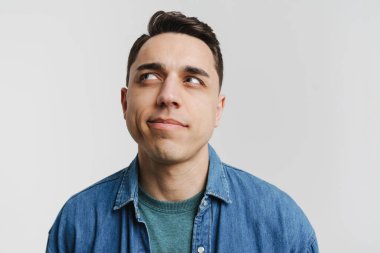 Genç esmer beyaz adam beyaz arka planda yalnız poz veriyor ve yan bakıyor.