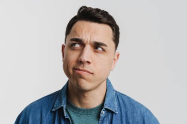 Genç esmer beyaz adam beyaz arka planda yalnız poz veriyor ve yan bakıyor.