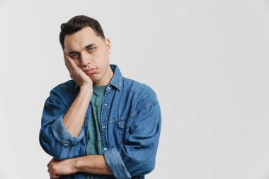 Genç esmer adam beyaz arka planda yalnız başına başını dik tutarken kameraya bakıyor.