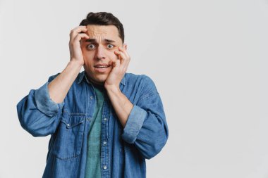 Genç esmer adam beyaz arka planda yüzünü kapatan kot gömlekli.