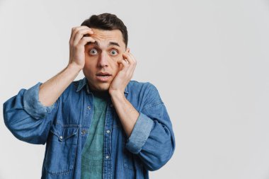 Genç esmer adam beyaz arka planda yüzünü kapatan kot gömlekli.