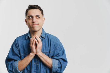 Genç esmer adam avuçlarını bir arada tutuyor ve beyaz arka planda tek başına bir kenara bakıyor.