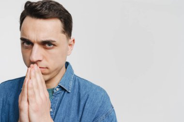 Genç esmer adam avuçlarını bir arada tutuyor ve beyaz arka planda izole edilmiş kameraya bakıyor.