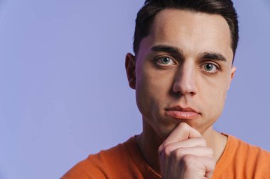 Genç esmer adam poz veriyor ve mor arka planda izole edilmiş kameraya bakıyor.