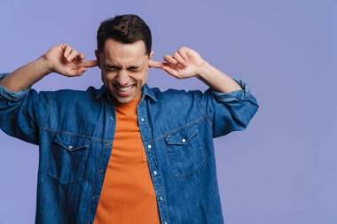 Genç esmer adam gülümsüyor ve kulaklarını tıkıyor.