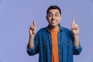 Genç esmer adam gülümsüyor ve parmaklarını tutuyor. Mor arka planda izole edilmiş.