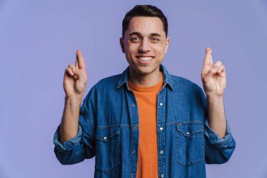 Genç esmer adam gülümsüyor ve parmaklarını tutuyor. Mor arka planda izole edilmiş.