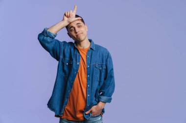 Genç esmer adam gülümsüyor ve parmağını yukarı kaldırıyor. Mor arka planda soyutlanmış.