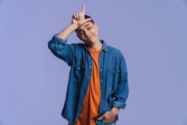 Genç esmer adam gülümsüyor ve mavi arka planda yalnız bir şekilde parmağını yukarı kaldırıyor.