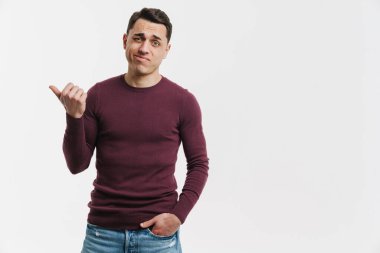 Genç esmer adam somurtuyor ve beyaz arka planda soyutlanmış bir şekilde işaret ediyor.
