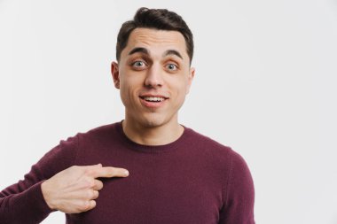 Genç esmer adam gülümsüyor ve beyaz arka planda kendini işaret ediyor.