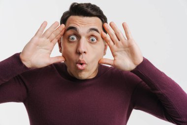 Genç esmer adam beyaz arka planda izole edilmiş kameraya bakıyor ve şaşırıyor.