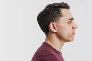 Genç esmer adam profilde poz veriyor ve beyaz arka planda soyutlanmış bir şekilde ileriye bakıyor.