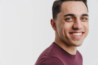 Genç esmer adam gülümsüyor ve beyaz arka planda izole edilmiş kameraya bakıyor.