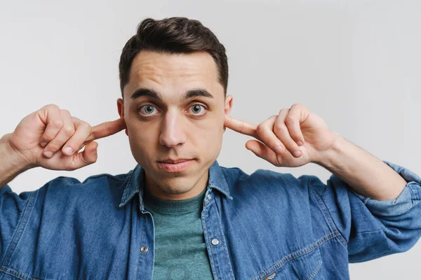 Genç esmer adam kameraya bakıyor ve beyaz arka planda kulaklarını tıkıyor.