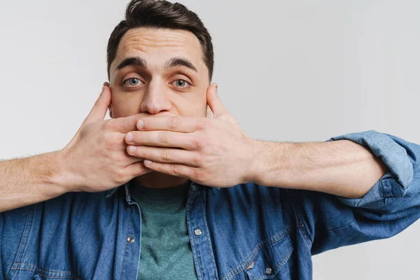 Genç esmer adam beyaz arka planda ağzını kapatan kot gömlekli adam.