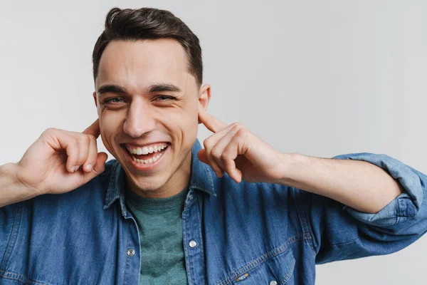 Genç esmer adam gülümsüyor ve kulaklarını tıkıyor.
