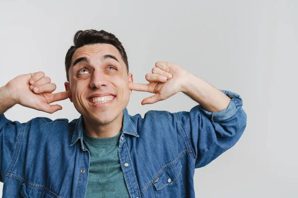 Genç esmer adam gülümsüyor ve kulaklarını tıkıyor.