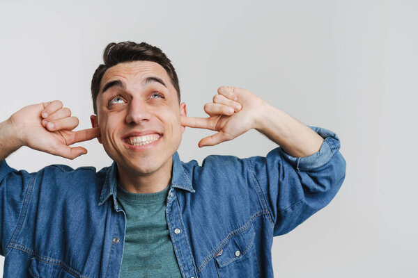Молодой брюнетка мужчина улыбается и затыкая уши изолированы на белом фоне
