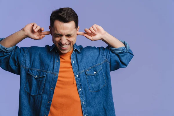 Genç esmer adam gülümsüyor ve kulaklarını tıkıyor.