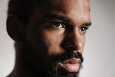 Siyah tişörtsüz sakallı adam beyaz arka planda yalnız poz veriyor ve yan tarafa bakıyor.