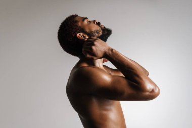 Siyah tişörtsüz sporcu esneme egzersizi yaparken beyaz arka planda tek başına çalışıyor.