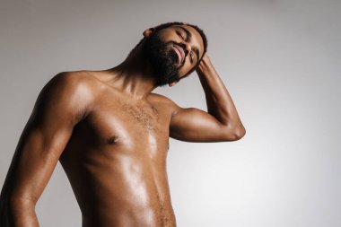 Siyah tişörtsüz sporcu esneme egzersizi yaparken beyaz arka planda tek başına çalışıyor.