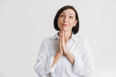 Avuç içlerini bir arada tutarken gülümseyen Avrupalı olgun kadın beyaz duvarın üzerinde izole halde.